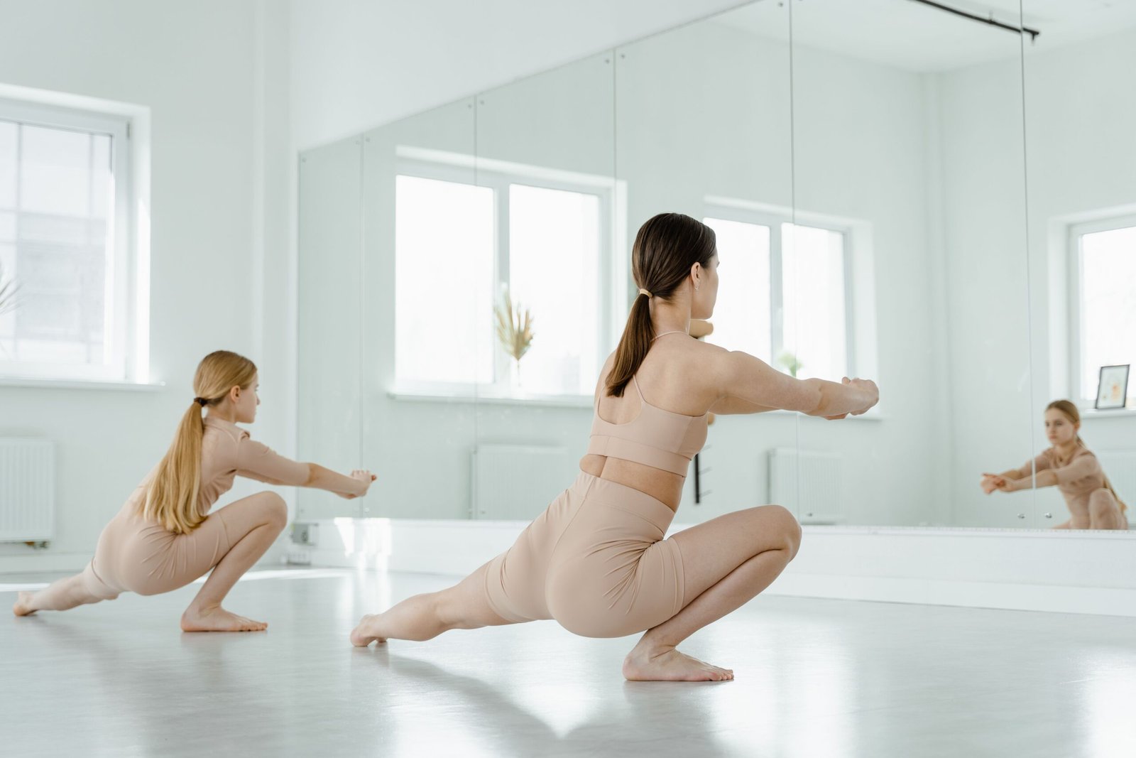 Two women stretching and dancing in a bright studio, reflecting in mirrors.