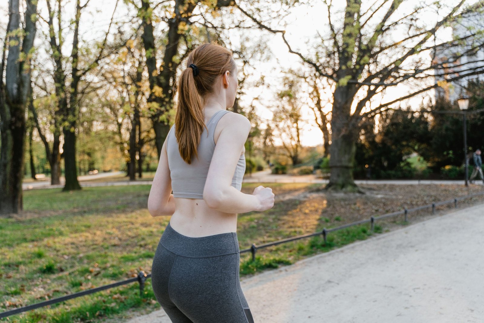 A woman jogs in a park during sunset, enjoying an outdoor fitness routine.
